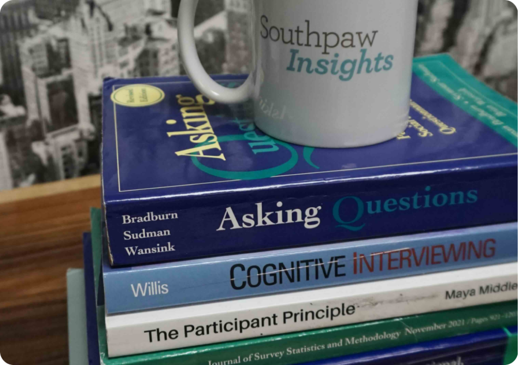 A mug with the text 'southpaw insights' perched atop a neat stack of research and interview-themed books, symbolizing a moment of reflection or study break amidst a background of research work.
